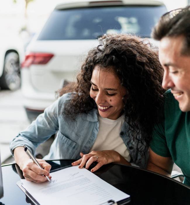 Mid adult couple signing documents to buy a car at dealership